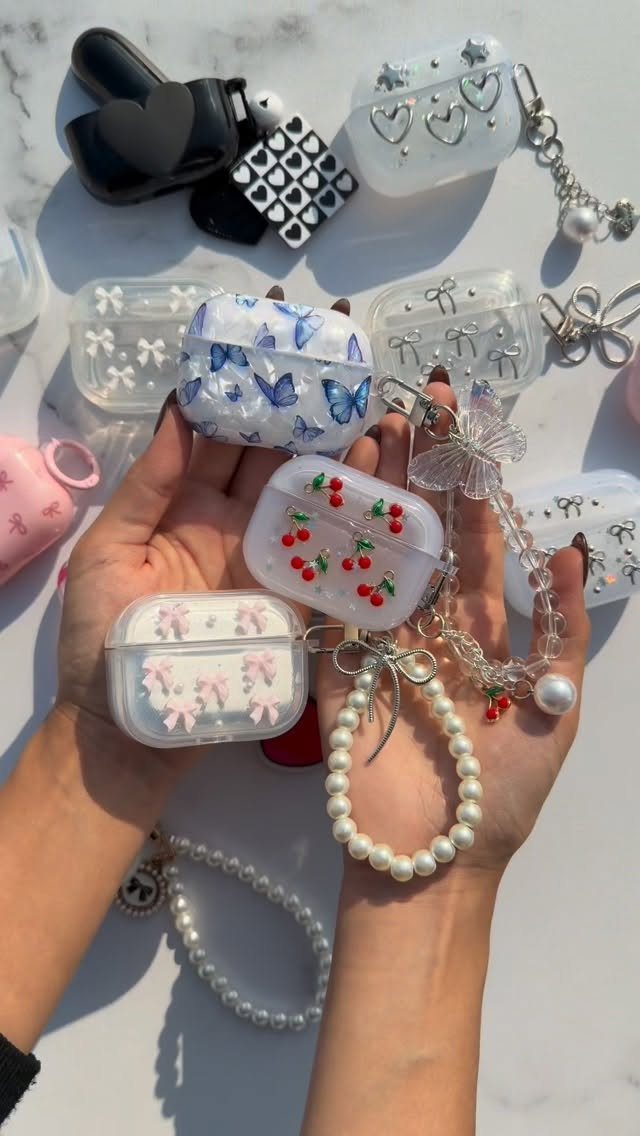 Decorative AirPods cases with cherries and butterflies held in a person's hands.