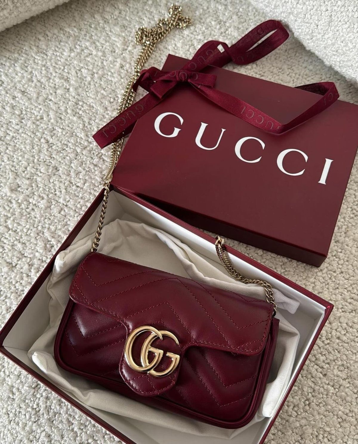 Burgundy quilted Gucci handbag with gold logo in a matching gift box.