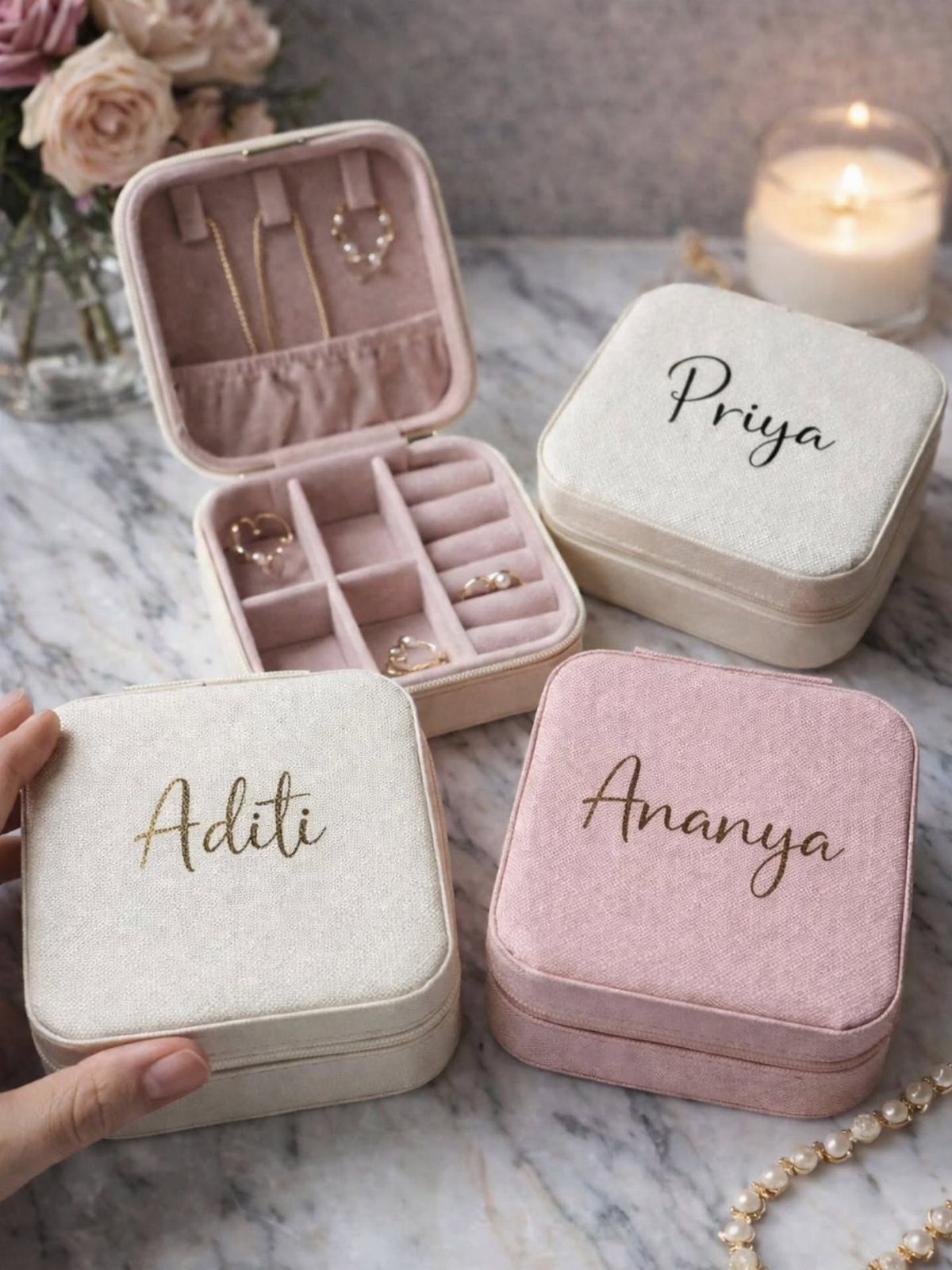 Three personalized velvet jewelry boxes with engraved names on a marble tabletop.