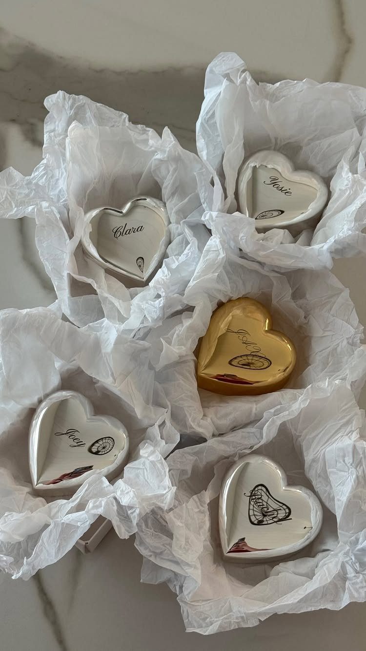 Heart-shaped ceramic trinket dishes with personalized names resting in white tissue paper.