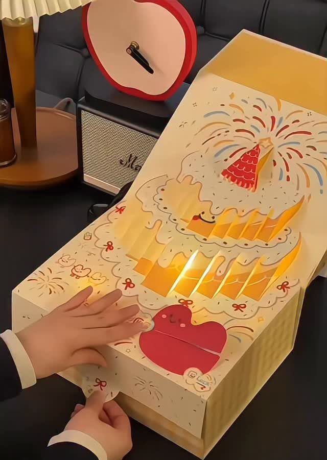 Pop-up gift box revealing a glowing 3D paper birthday cake with a party hat.