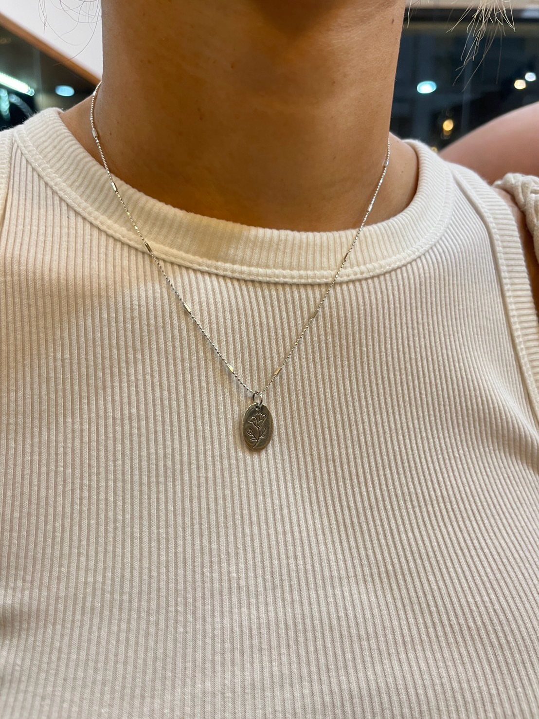 Silver oval pendant necklace worn on a person wearing a white ribbed top