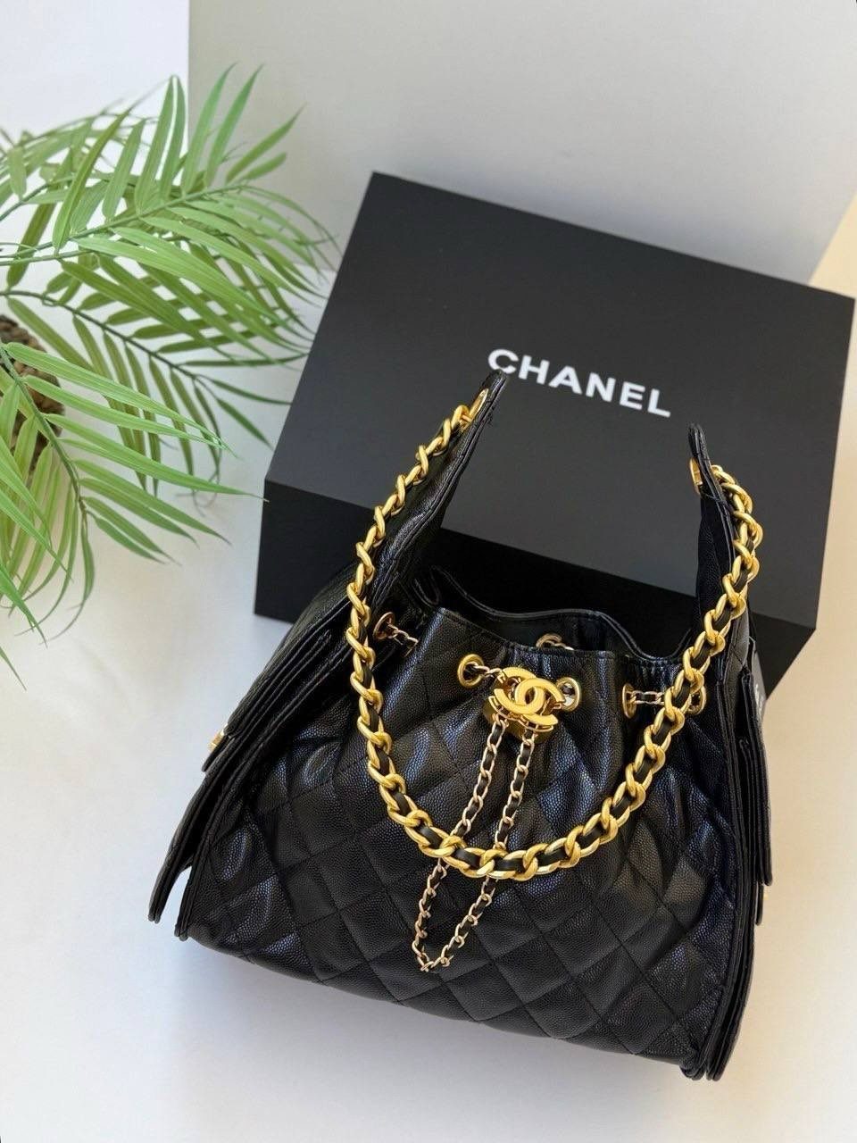 Black quilted leather handbag with gold chains next to a Chanel gift box.