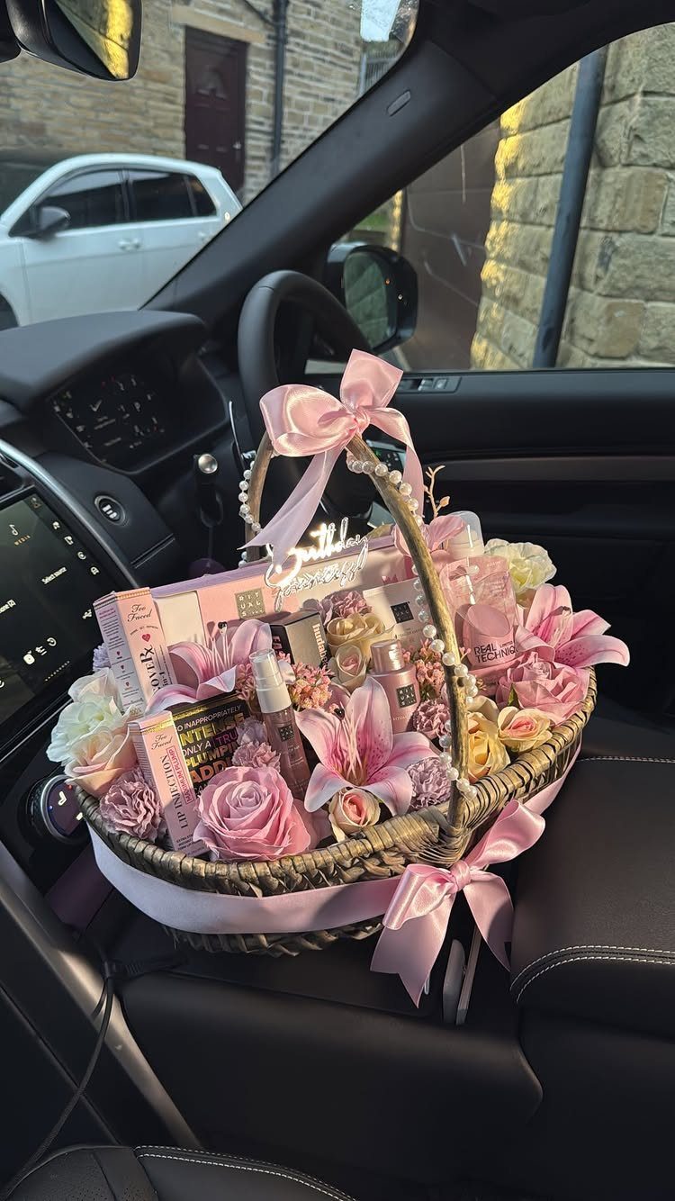 Wicker gift basket with pink flowers and beauty products on a car seat
