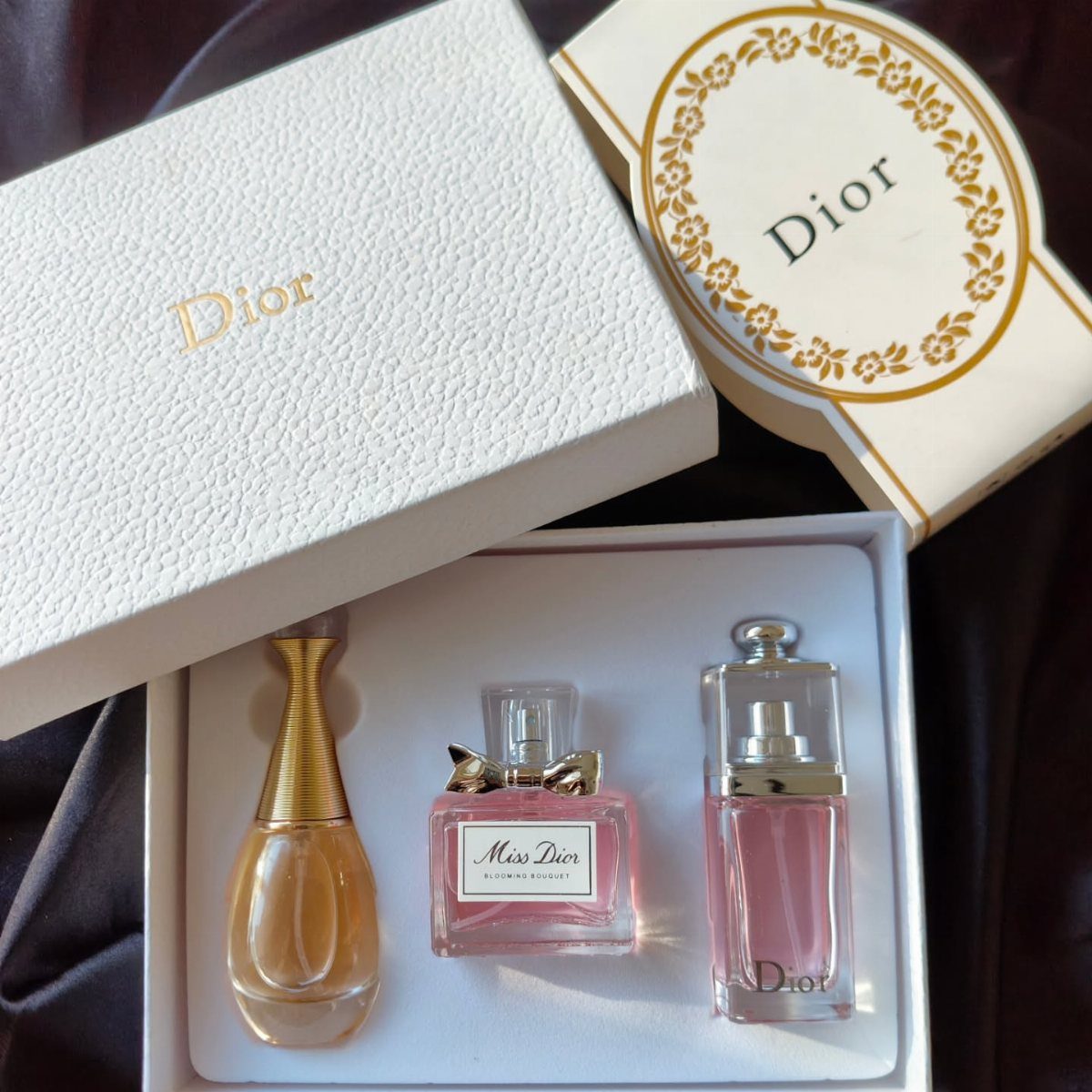 Three Dior perfume bottles in a white gift box on a dark surface
