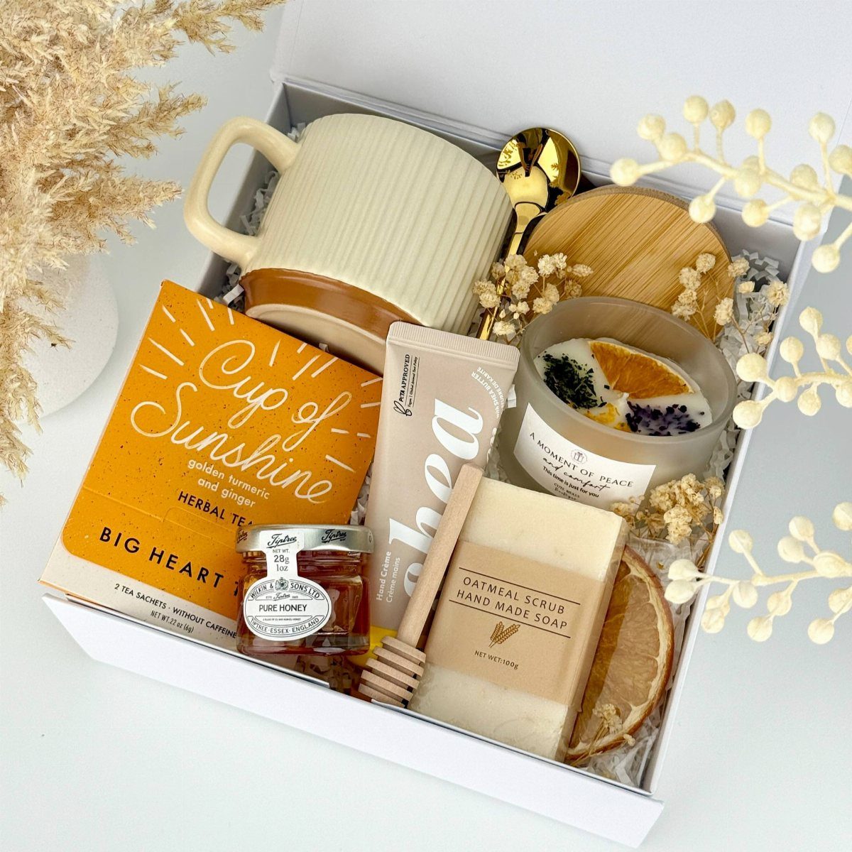 Gift box with a ribbed mug, herbal tea, honey, soap, and a candle.