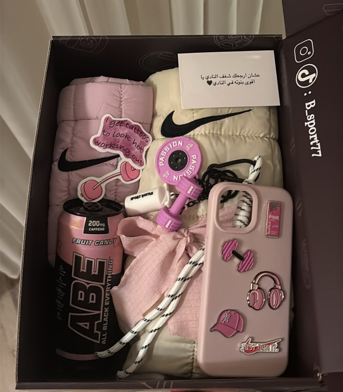 Fitness gift box with pink dumbbells, Nike athletic wear, and energy drink.