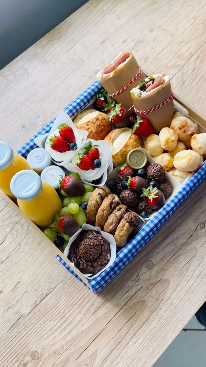 Gourmet food basket with wraps, pastries, fresh fruit, and juice in checkered tray.