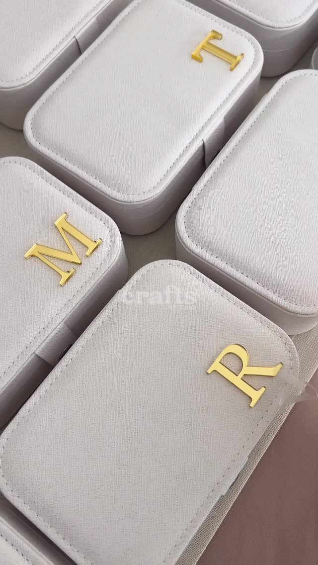 Light grey fabric jewelry boxes with gold metallic initial letters on the lids.