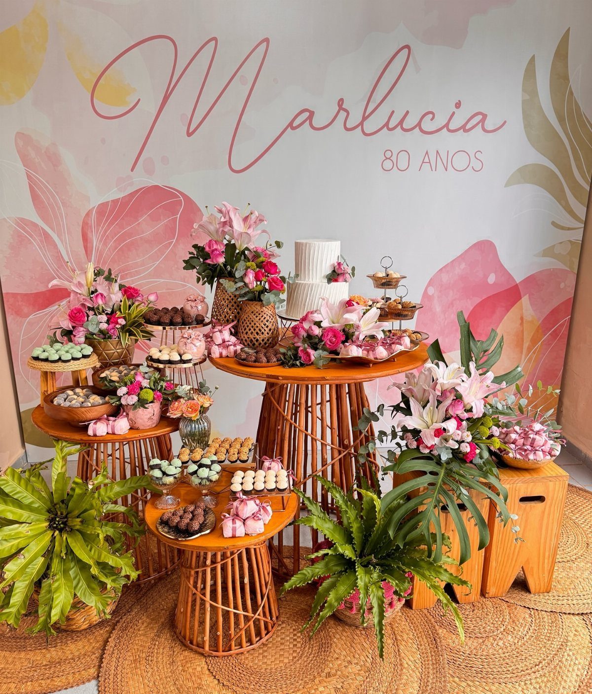 Floral arrangements with pink and white lilies on wooden tables for an 80th birthday.