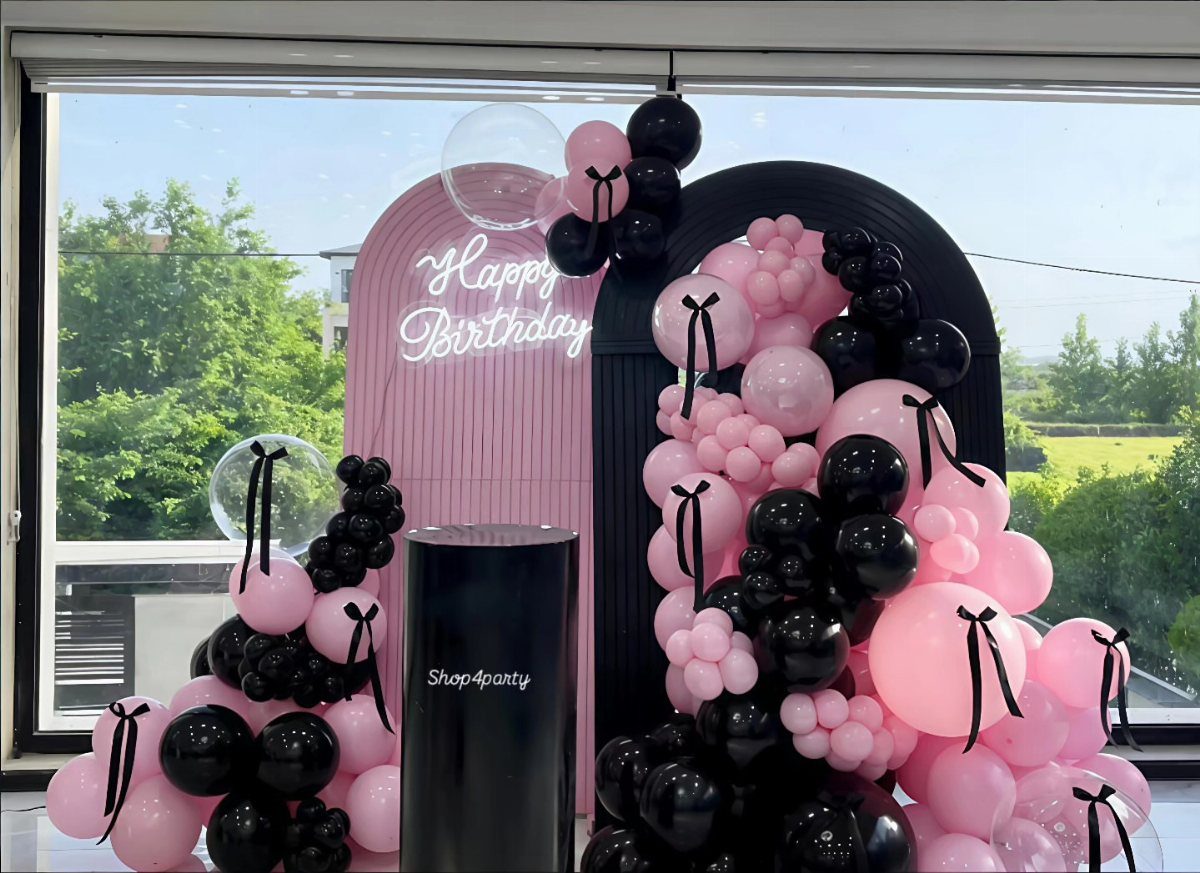 Pink and black latex balloons decorating a birthday party backdrop with neon signage.