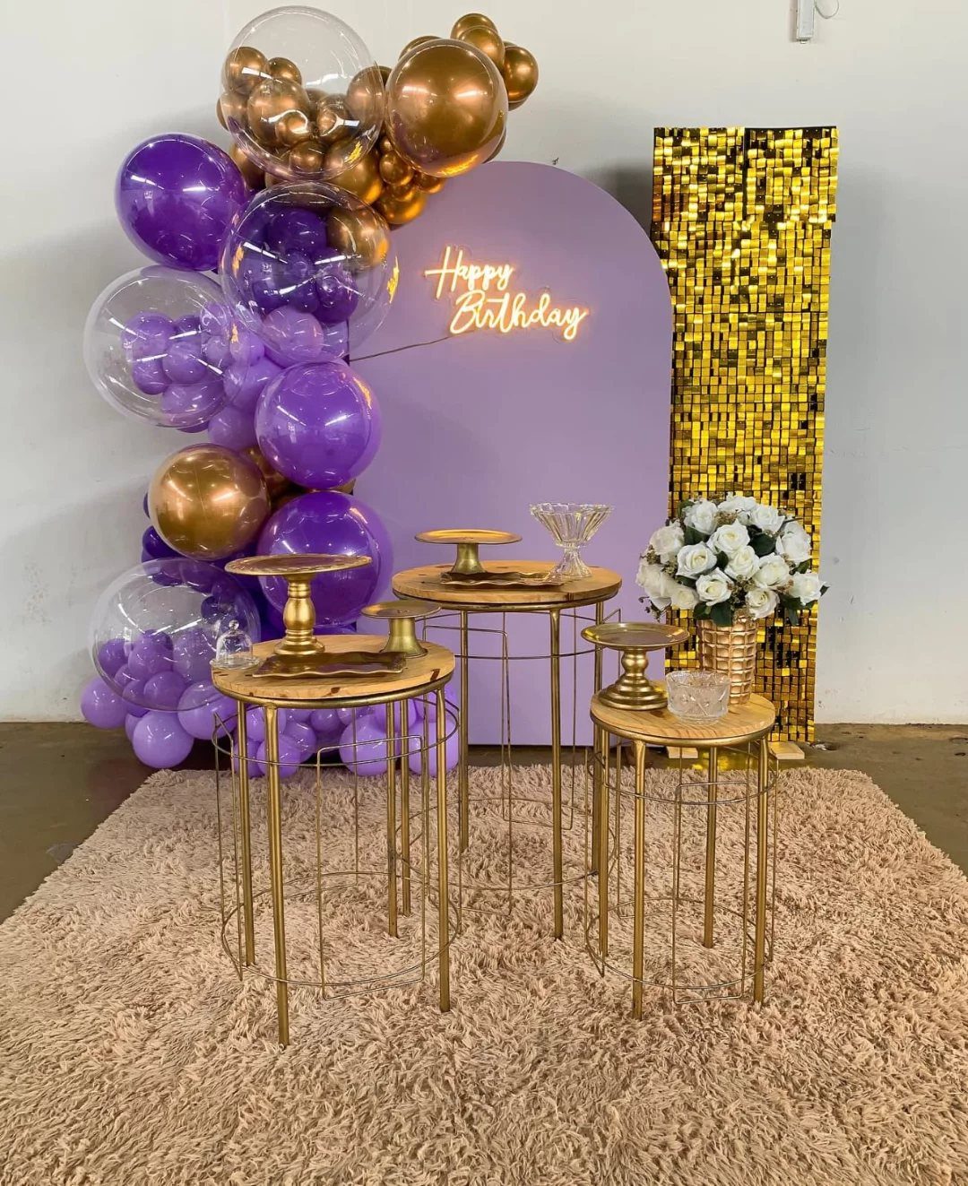 Purple and gold balloon arch with gold pedestal tables and neon birthday sign.