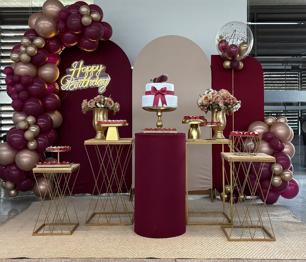 Burgundy and cream balloons surrounding a birthday cake on gold pedestals.