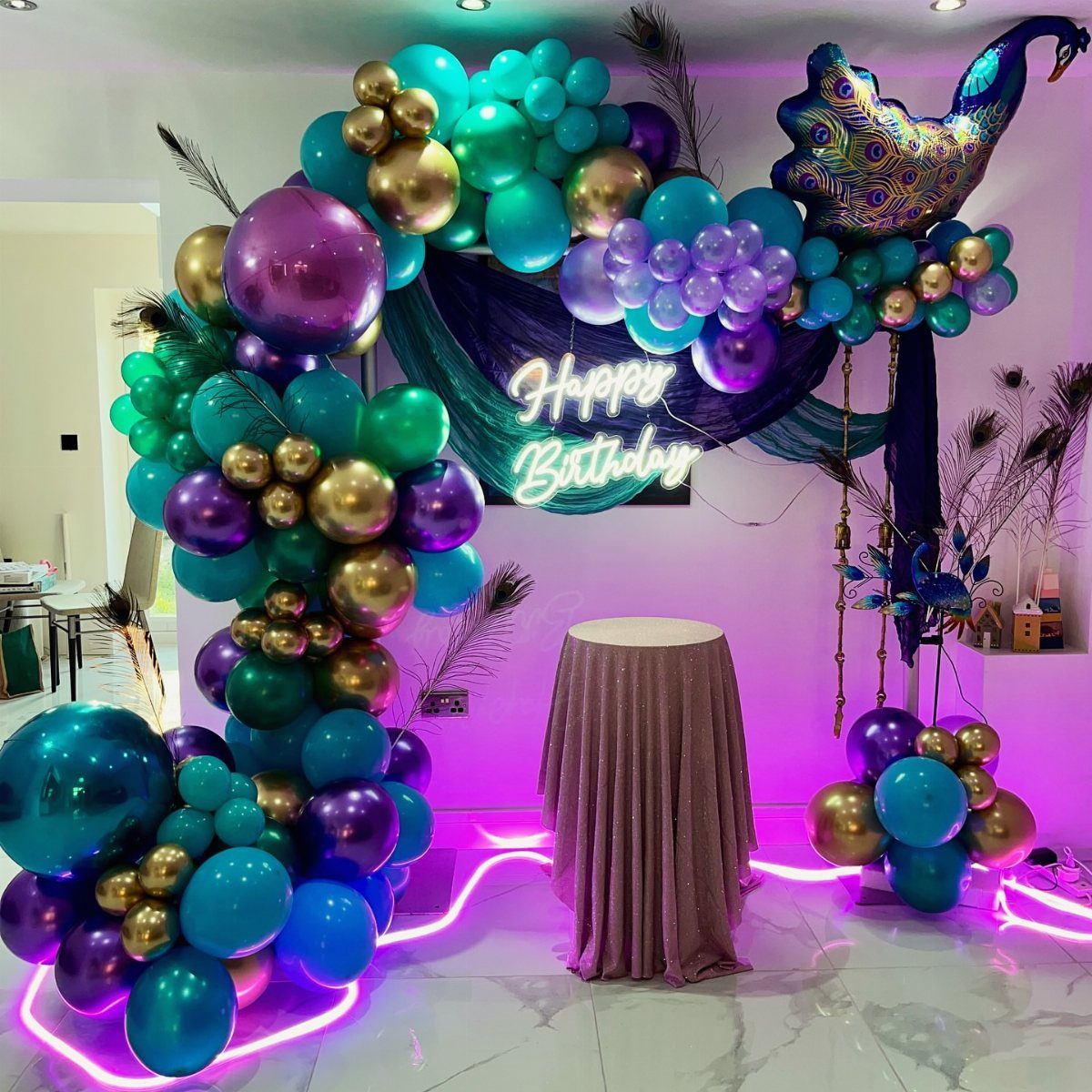 Emerald green and gold balloon arch with purple accents and neon birthday sign.