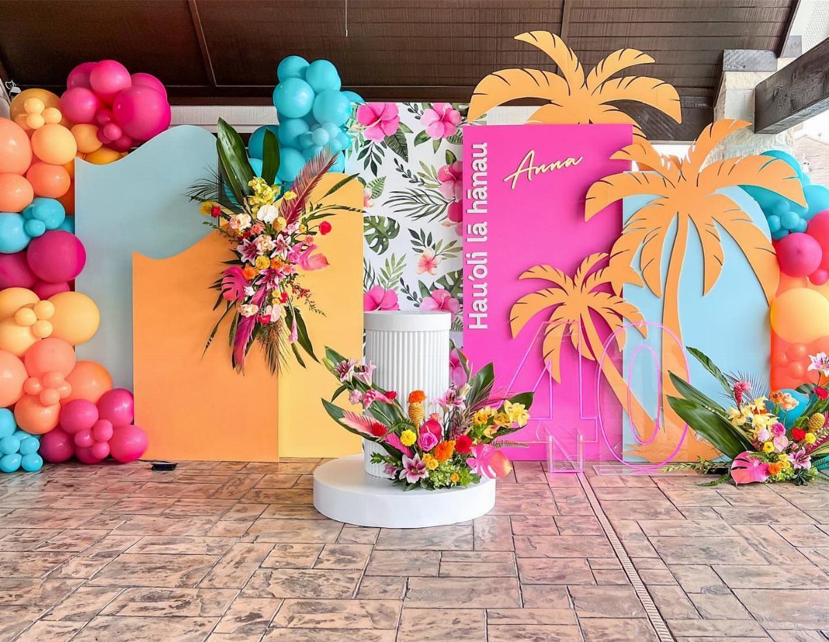 Tropical party backdrop with orange, pink, and blue decorations and floral arrangements.