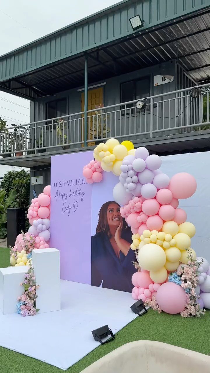 Pastel pink, yellow, and lavender balloon arch surrounding a purple birthday backdrop.