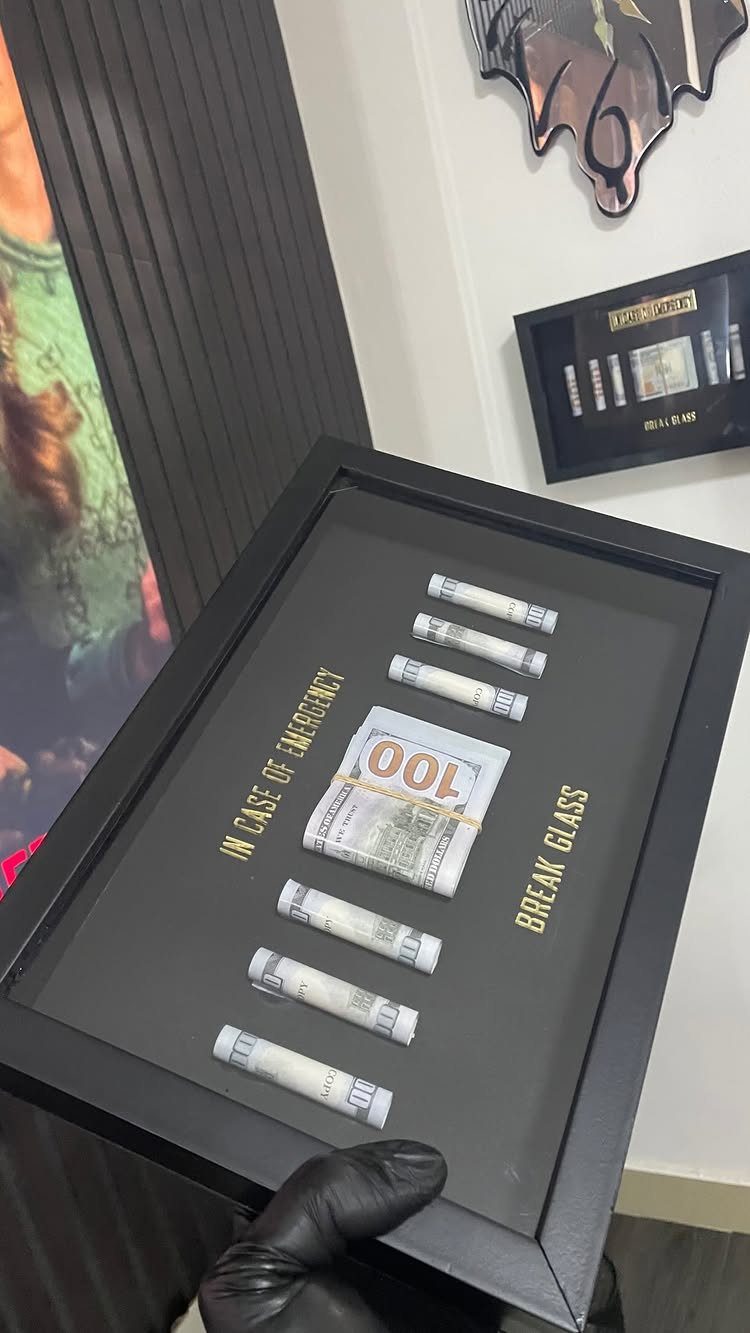 Black shadow box with money and gold text saying break glass in case of emergency