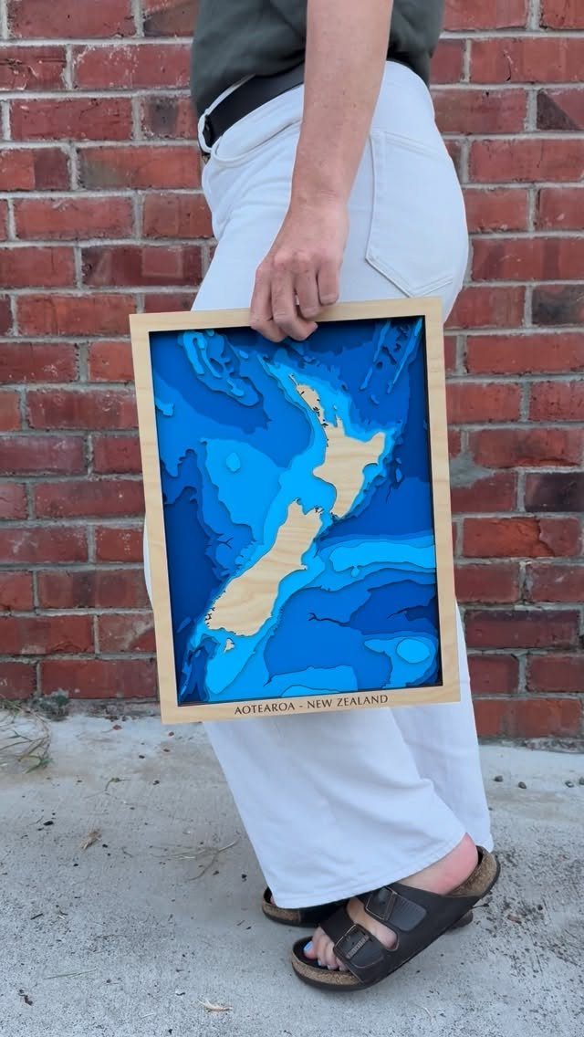 Wooden framed 3D topographic map of New Zealand held by a person.