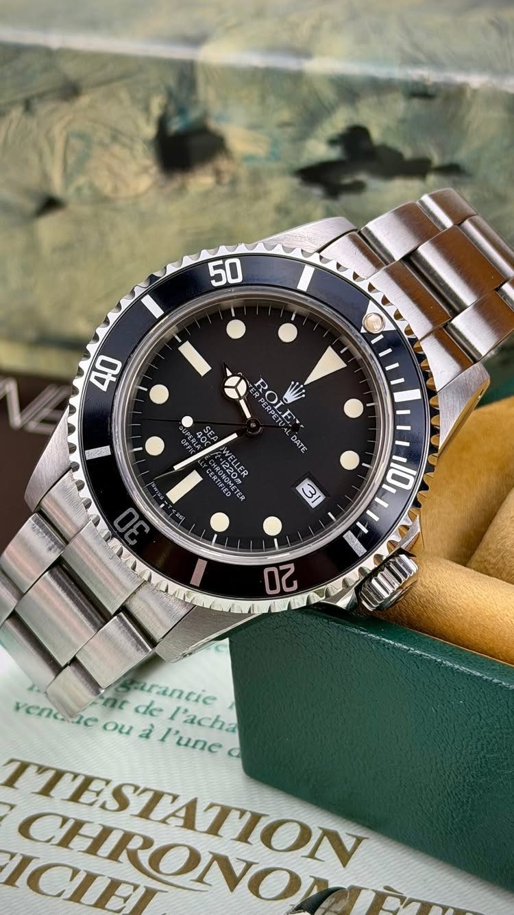 Silver Rolex dive watch with black dial resting on a green leather box.