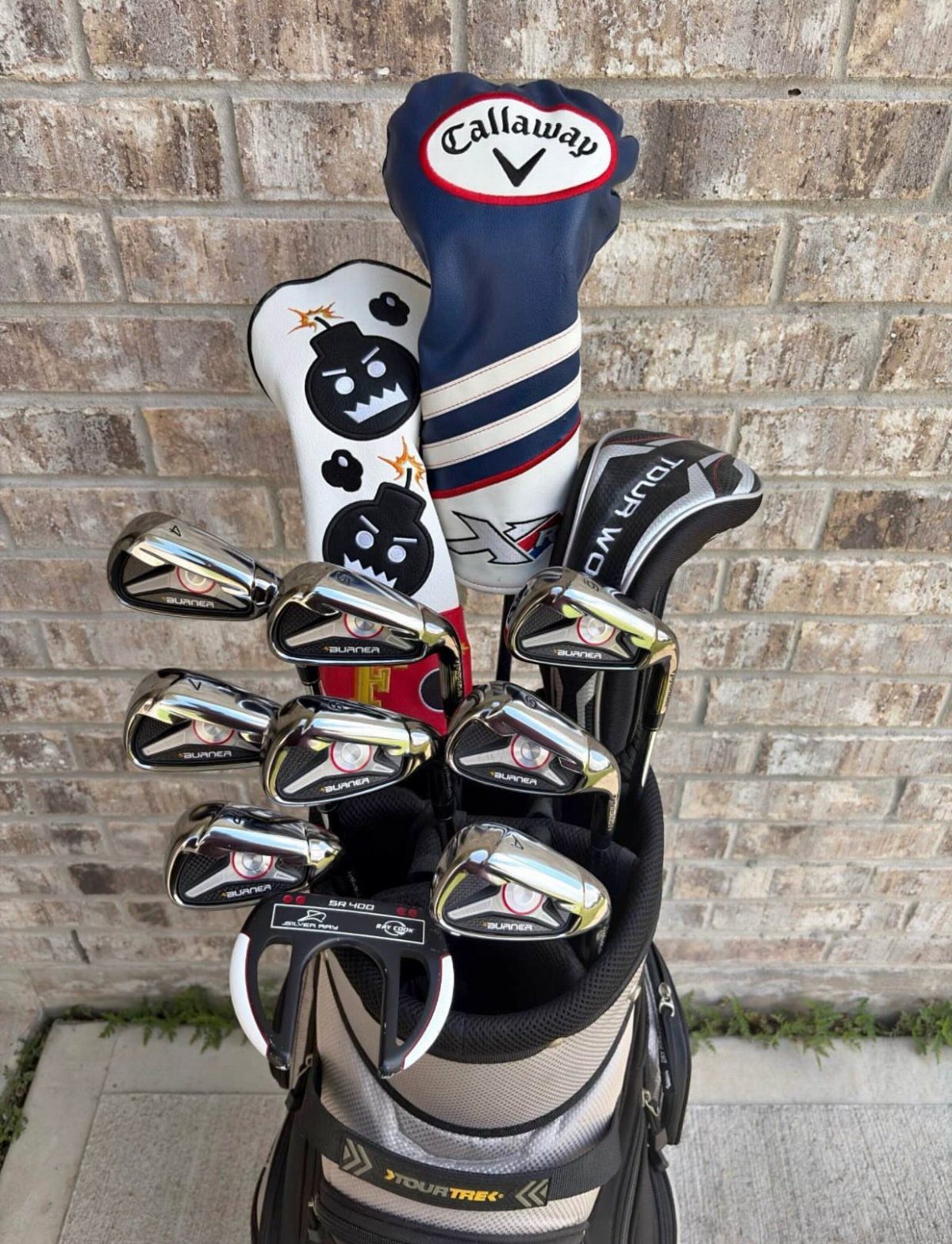 Golf club set in a TourTraits bag leaning against a brown brick wall.