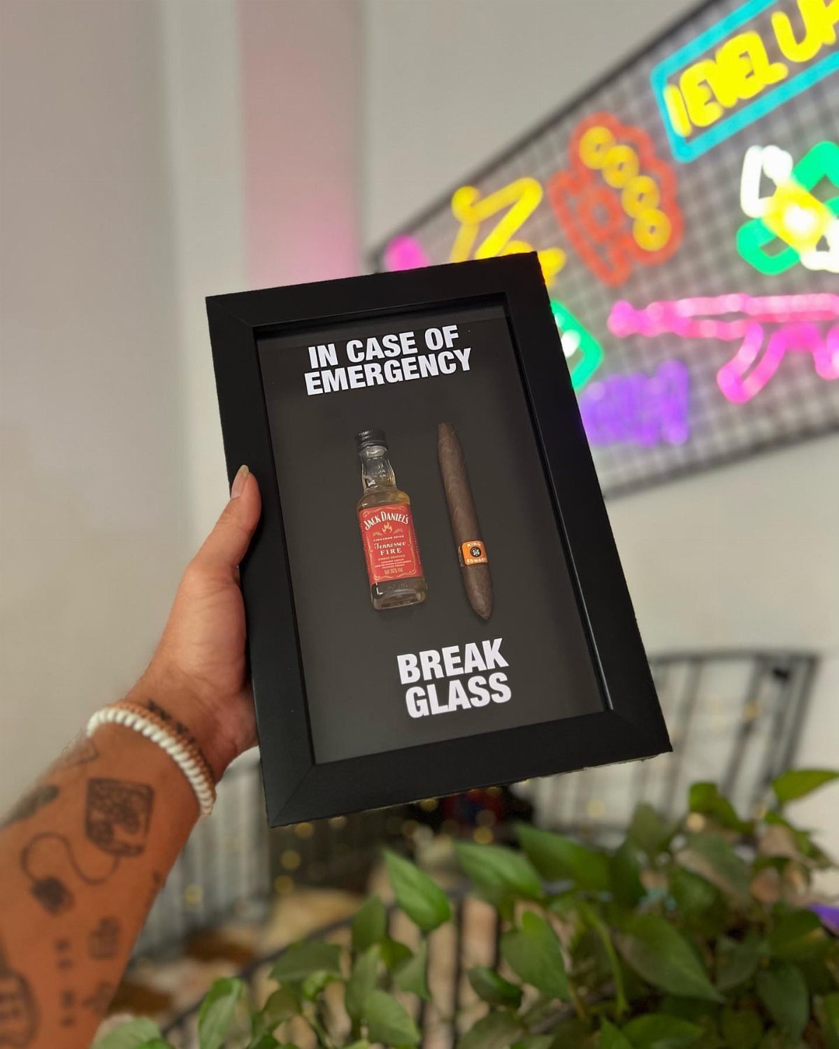 Shadow box frame containing a small liquor bottle and a cigar for emergencies.