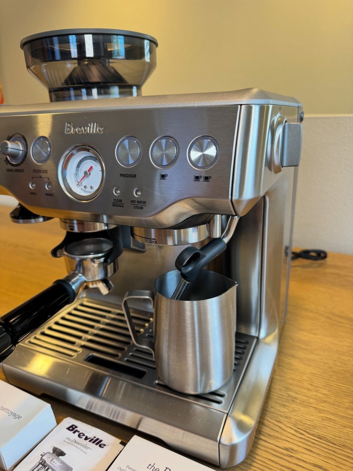 Stainless steel Breville espresso machine with a metal milk pitcher on wooden table