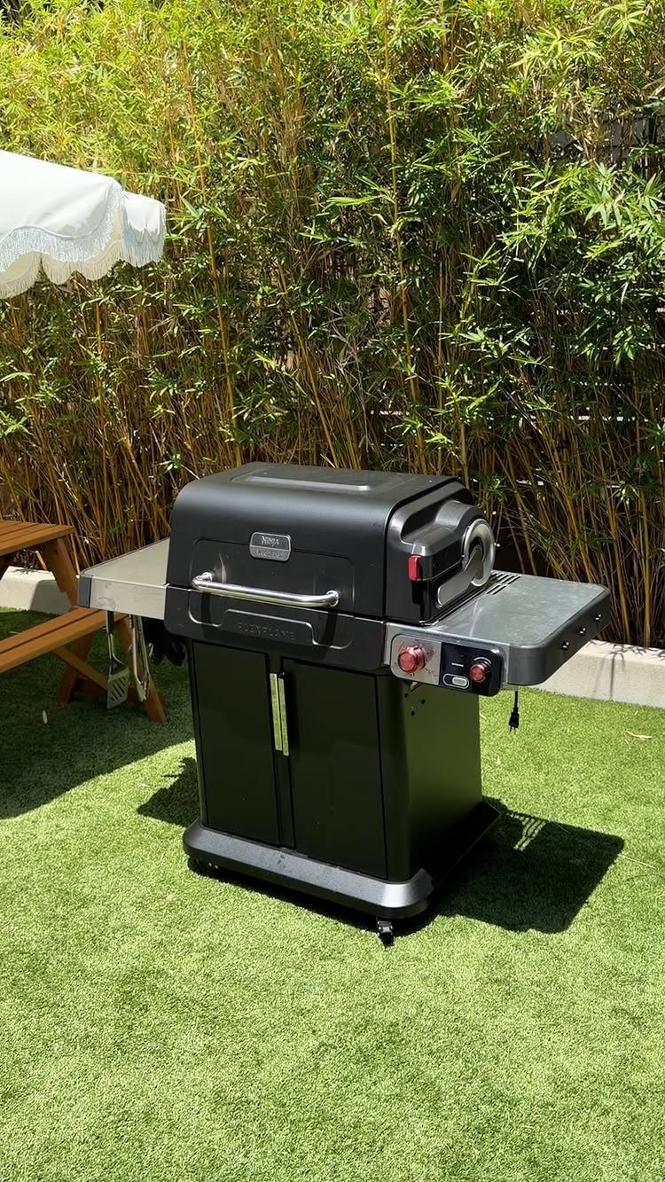 Black pellet grill standing on green artificial grass against a bamboo hedge background
