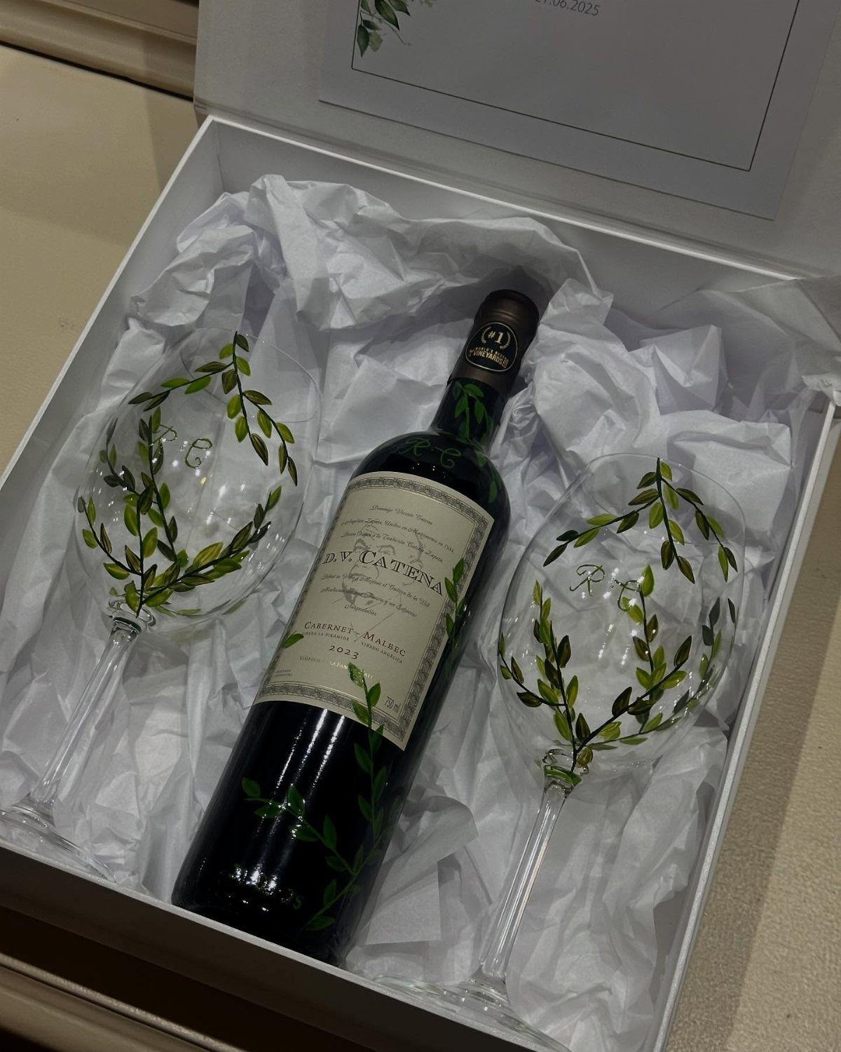 Bottle of red wine and two leaf-patterned wine glasses in a white gift box