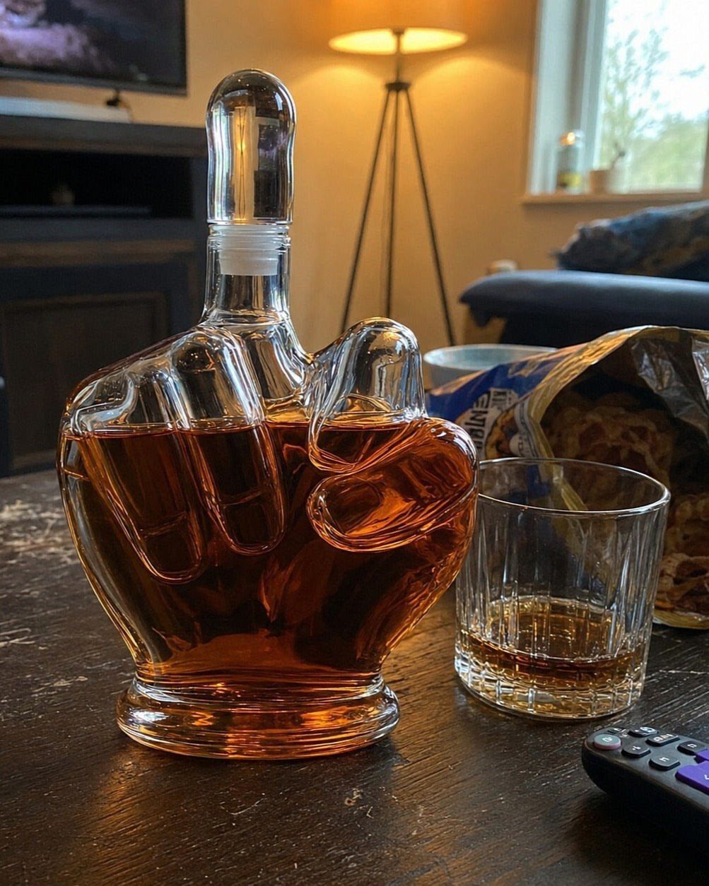 Fist-shaped glass whiskey decanter filled with amber liquor next to a whiskey glass.