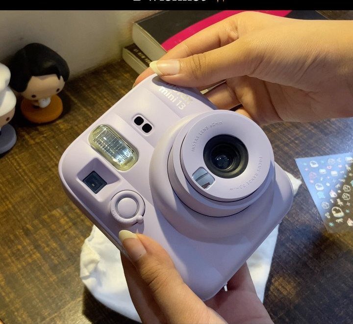 Light purple instant camera held by two hands over a wooden table.