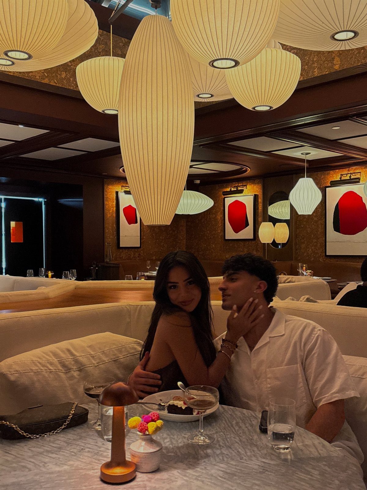 Young couple sitting in a booth at a restaurant with large oval lights.