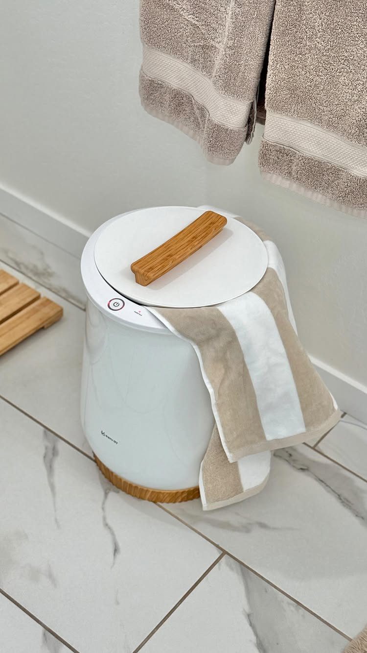 White cylindrical freestanding towel warmer with a wooden handle on marble flooring.