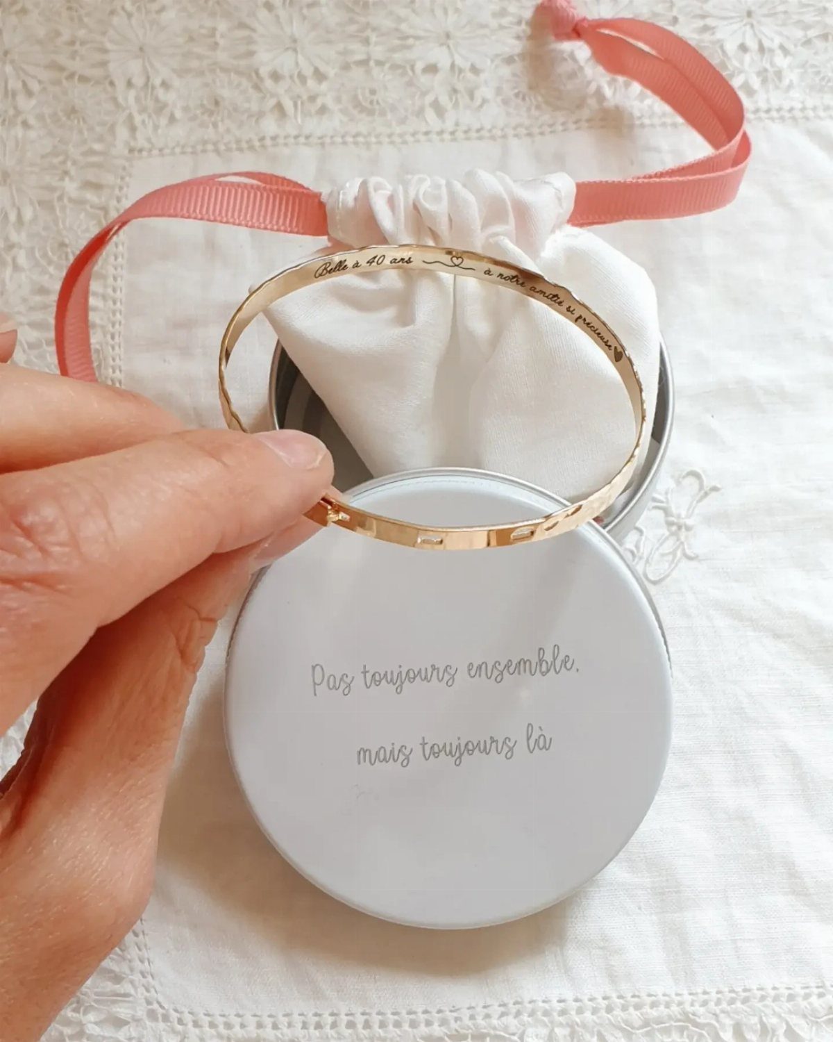 Gold engraved bangle bracelet held over a white gift tin and pouch.