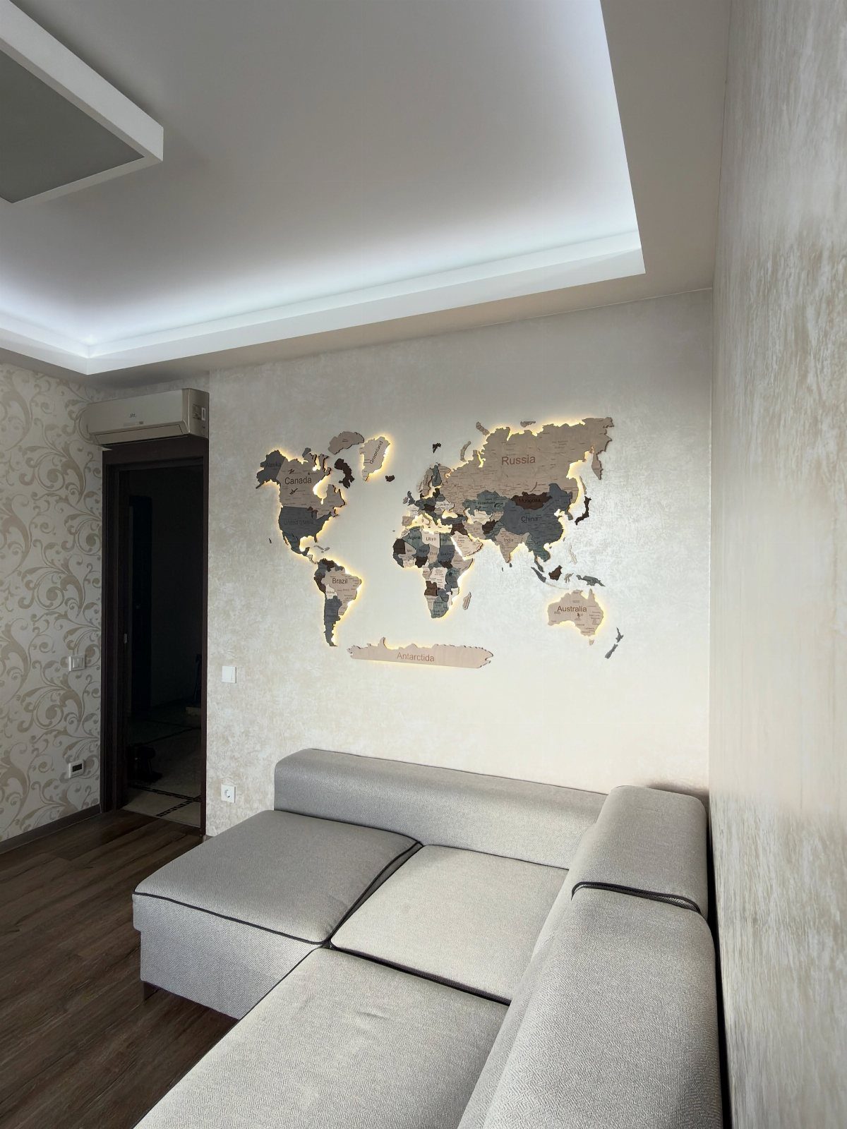 Backlit wooden world map mounted on a wall above a grey sectional sofa.