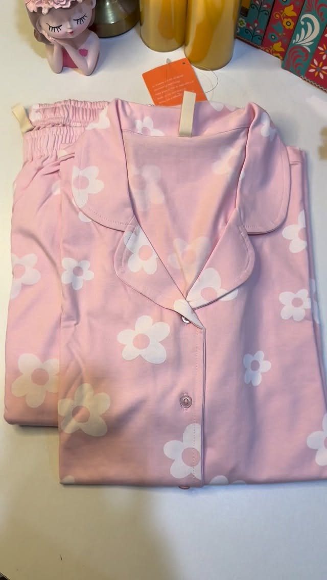 Pink floral pajamas set laid flat on a white table with decorative accessories.