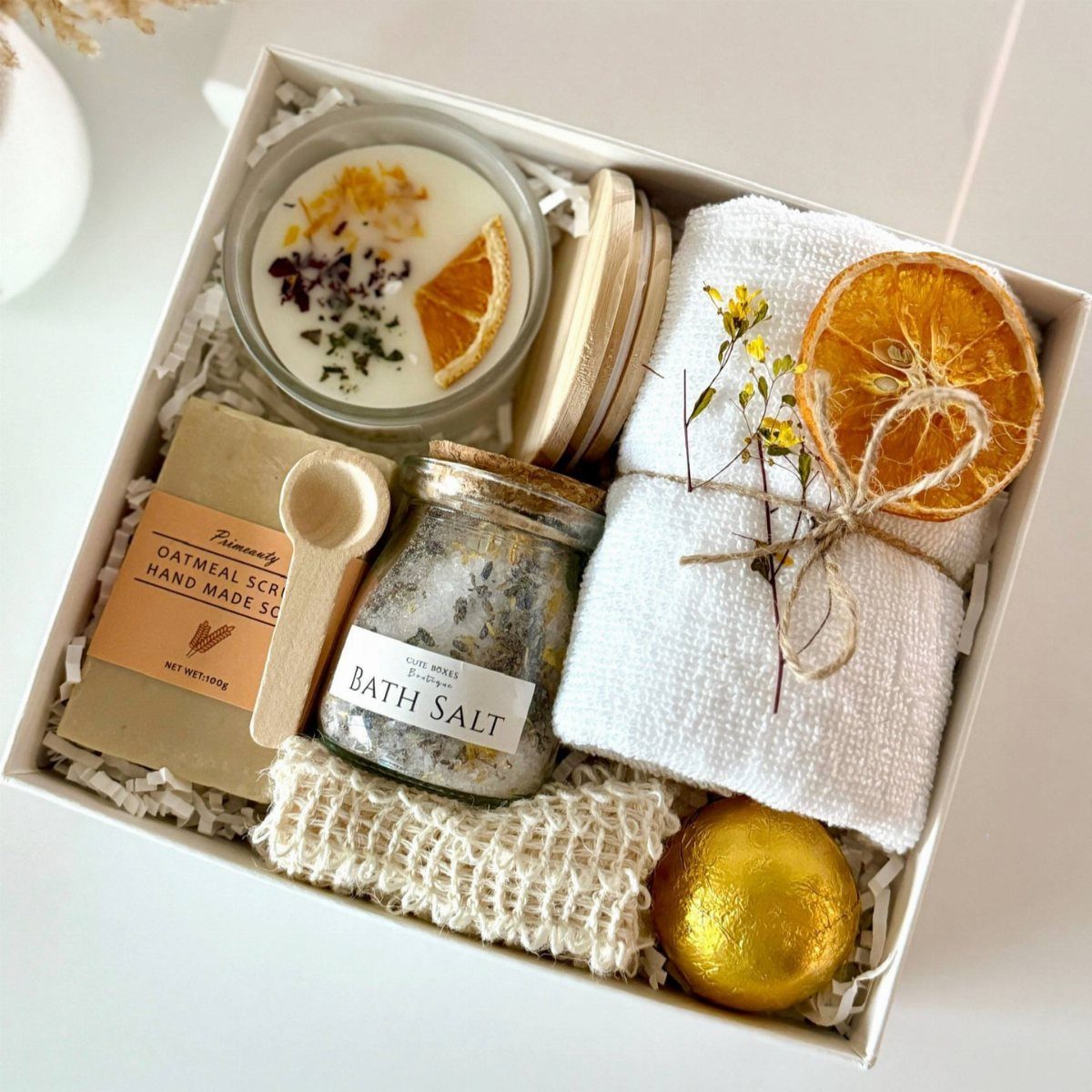 Self-care gift box with bath salts, candle, scrub, towel, and gold bath bomb.
