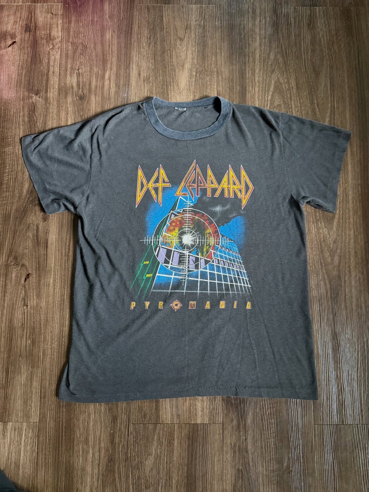 Grey vintage Def Leppard Pyromania t-shirt laid flat on a wooden floor.