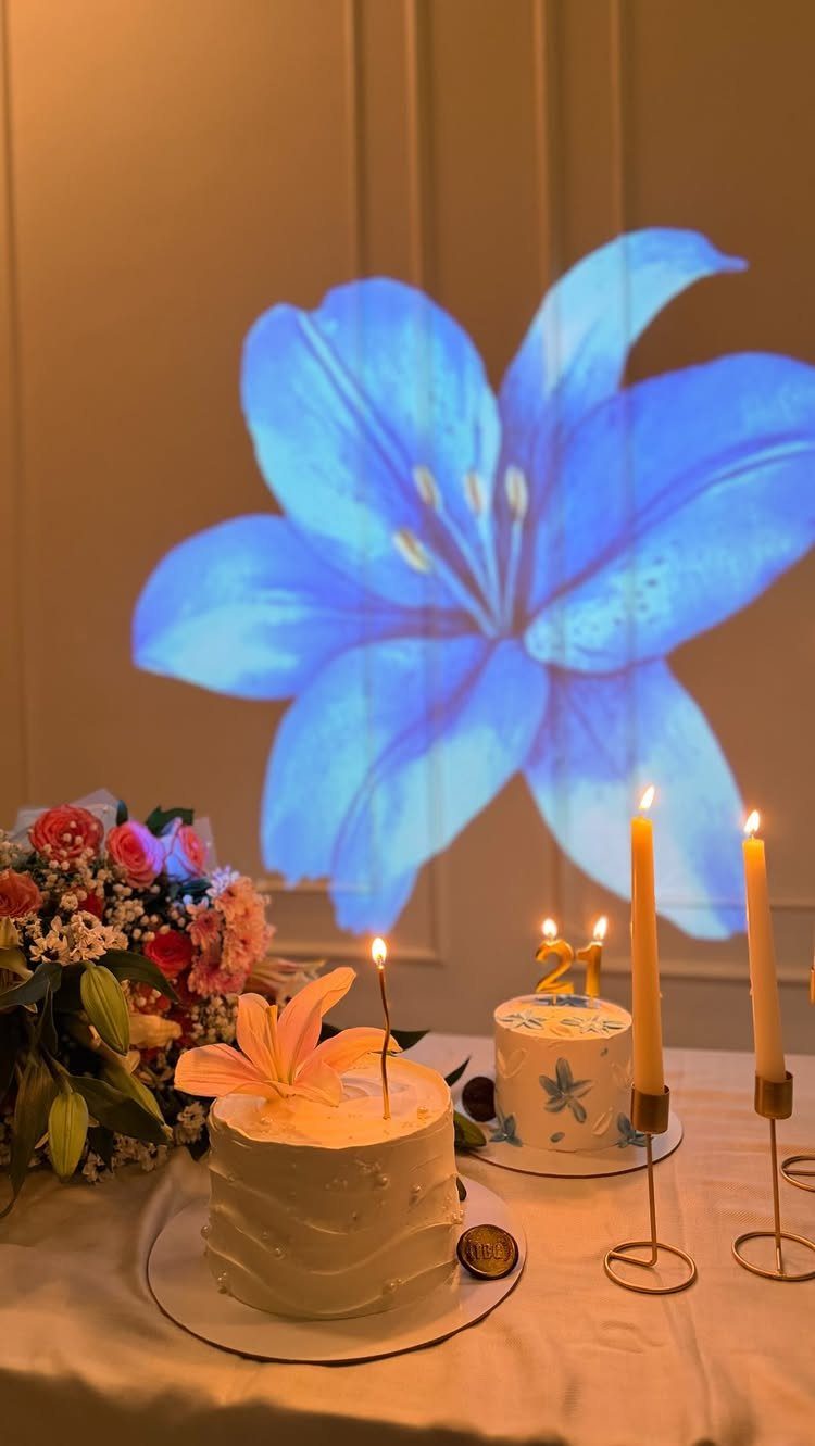 Two white birthday cakes with a 21 candle and blue lily projection.