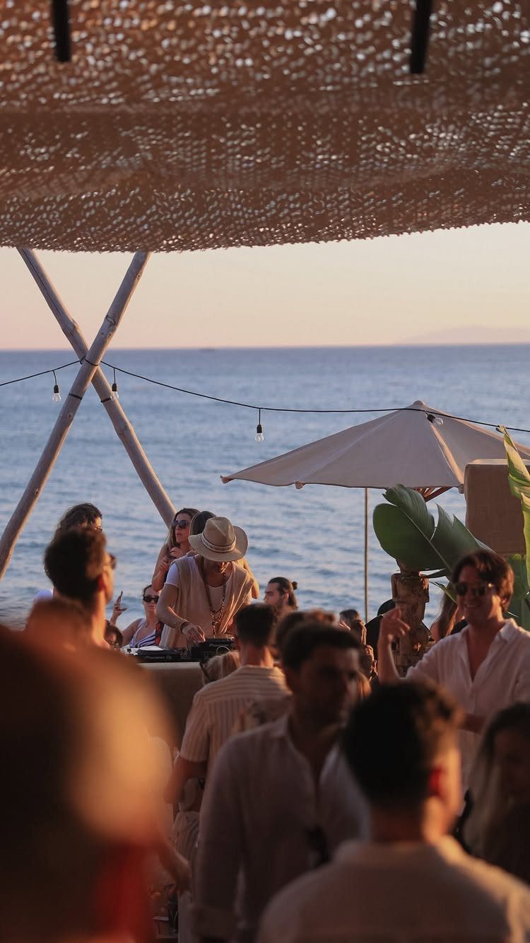 People gathering at a beach club with a DJ performing by the ocean.