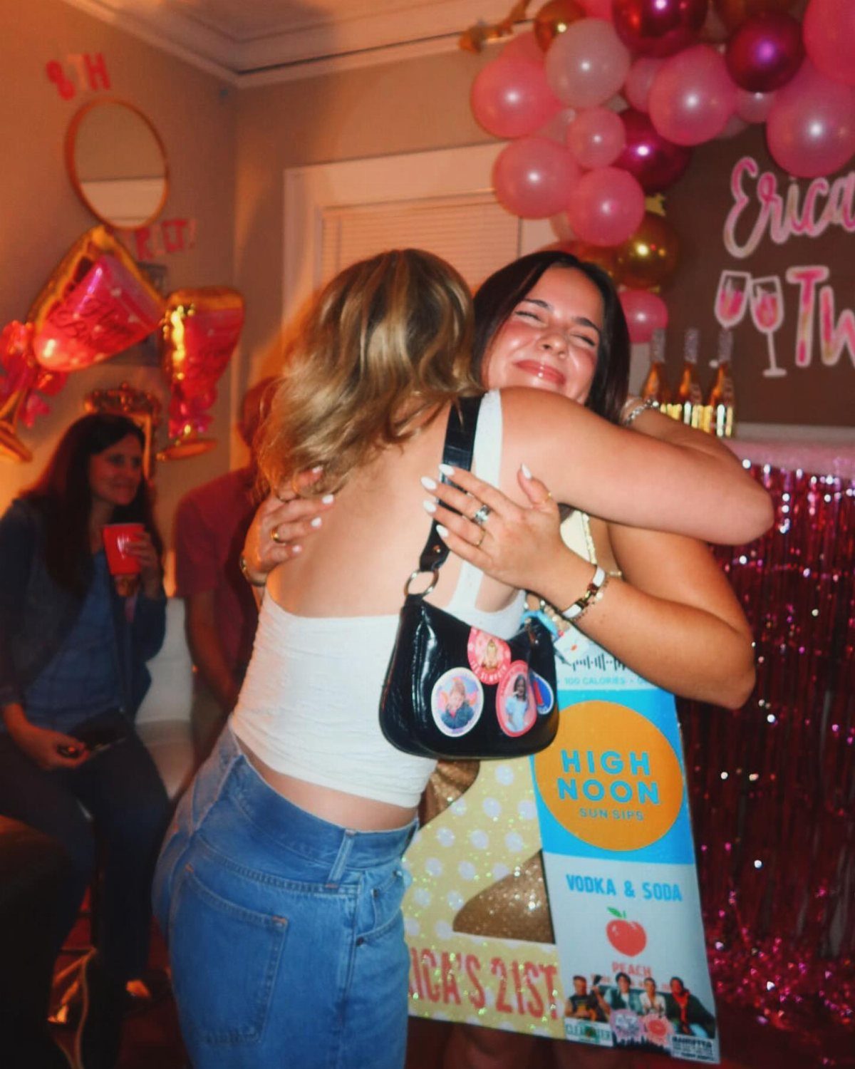 Two young women hugging at a 21st birthday party with pink balloons.