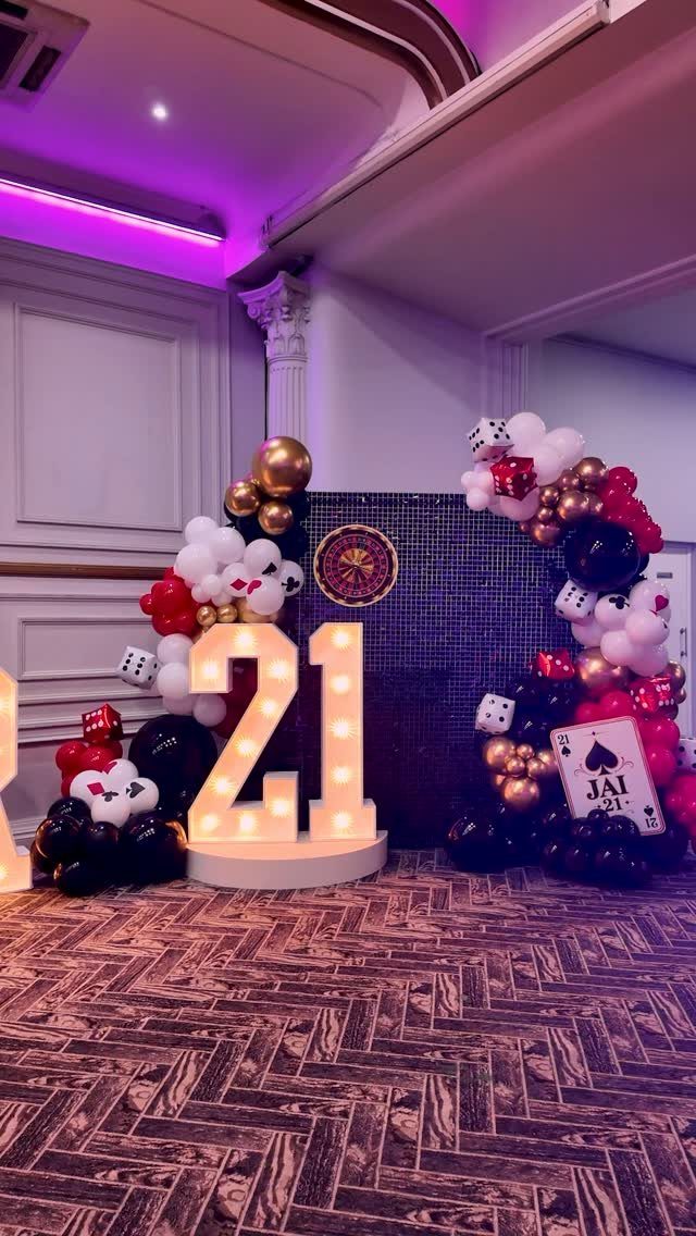 Illuminated number 21 surrounded by casino themed balloons, dice, and playing cards.