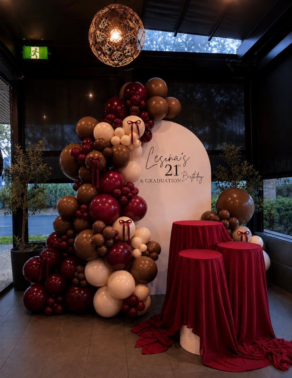 Balloon arch in burgundy and gold next to a 21st birthday backdrop.