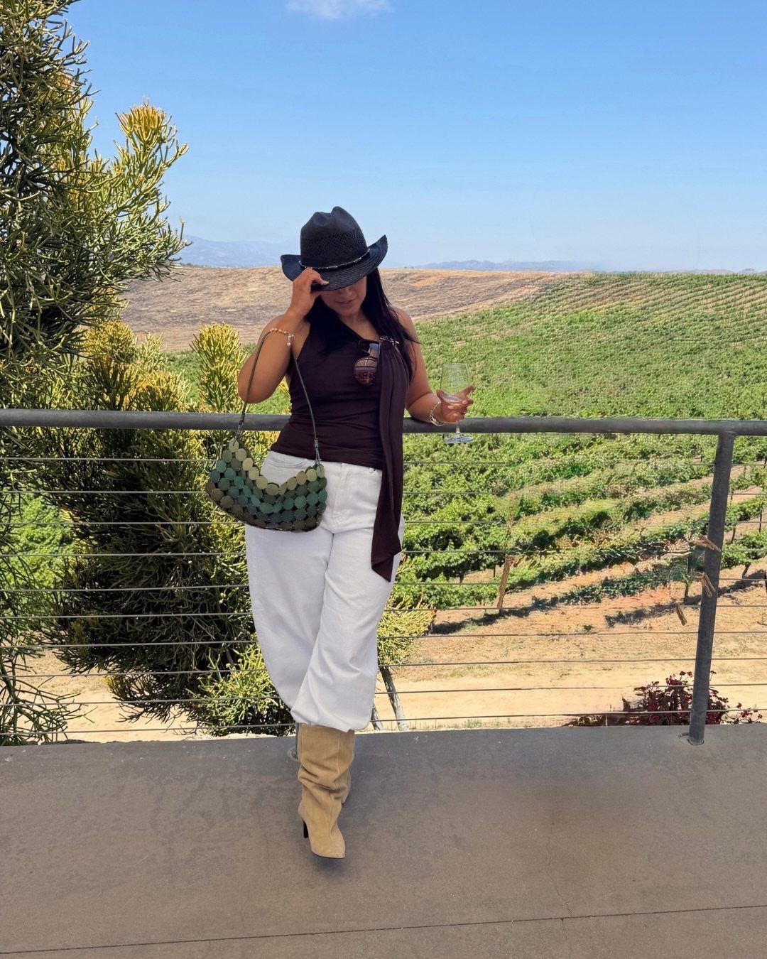 Woman holding a glass of wine overlooking a lush green vineyard landscape.