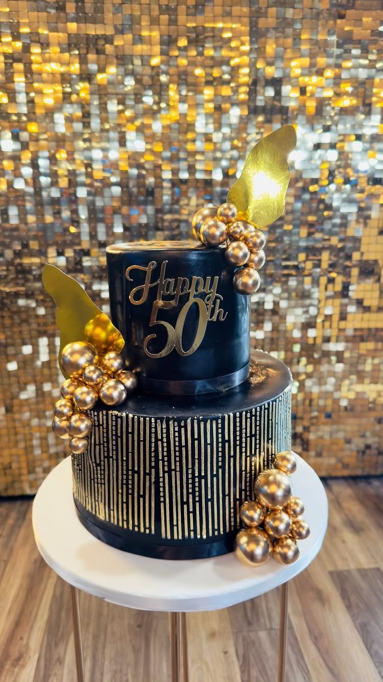 Two-tier black and gold 50th birthday cake on a white stand with gold backdrop