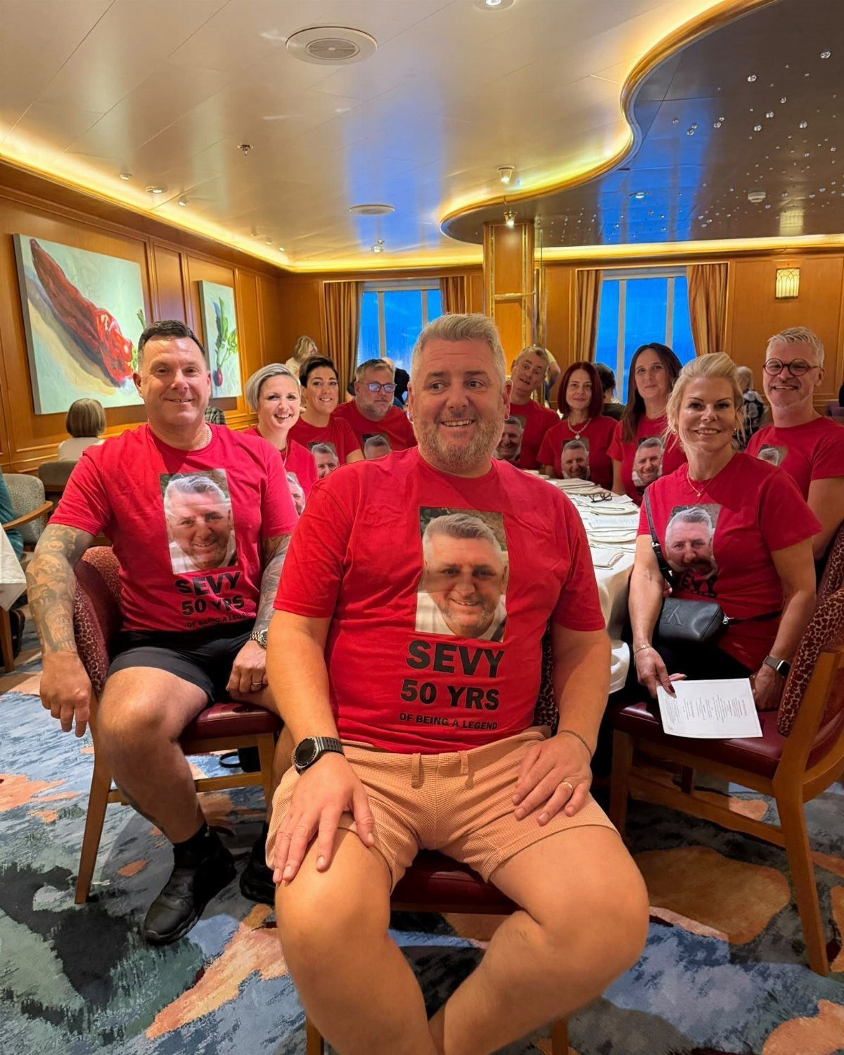 Group of people wearing matching red 50th birthday t-shirts in a lounge.