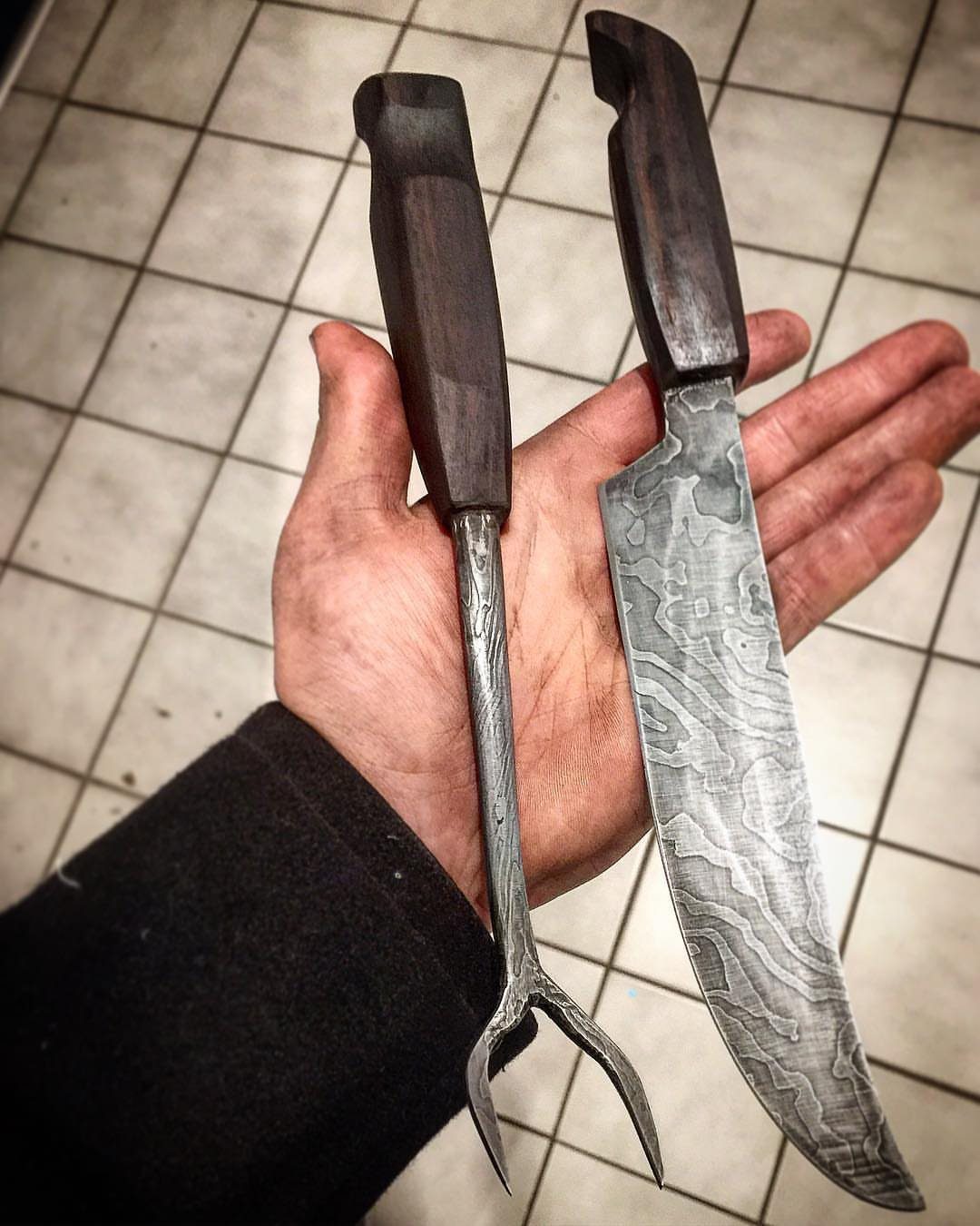 Damascus steel knife and carving fork with wooden handles held in a hand.