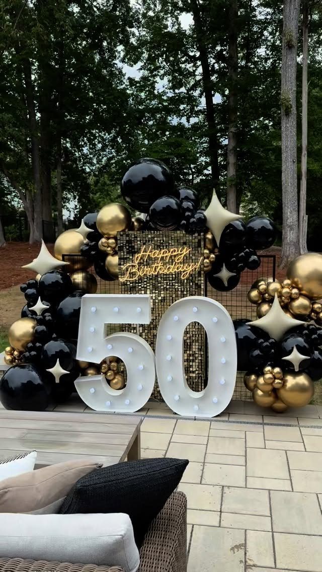 Large illuminated number 50 with black and gold balloons and sequin backdrop.