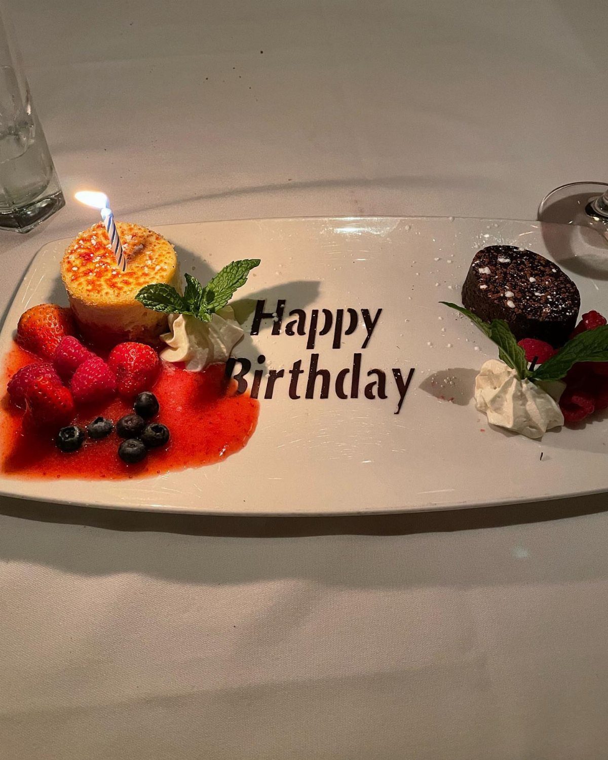 Birthday dessert plate with two cakes, fresh berries, and Happy Birthday written in chocolate.