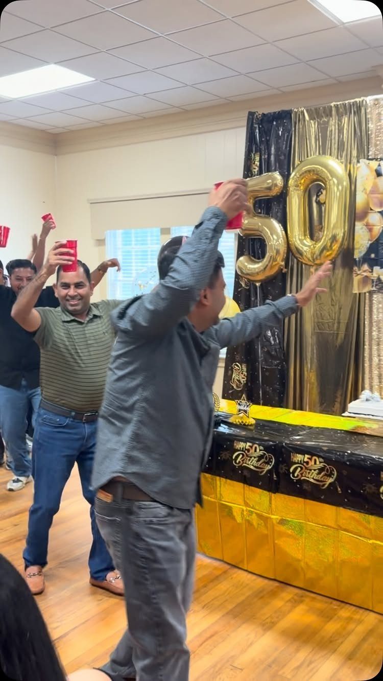 Men celebrating a 50th birthday with gold balloons and party decorations in a room.