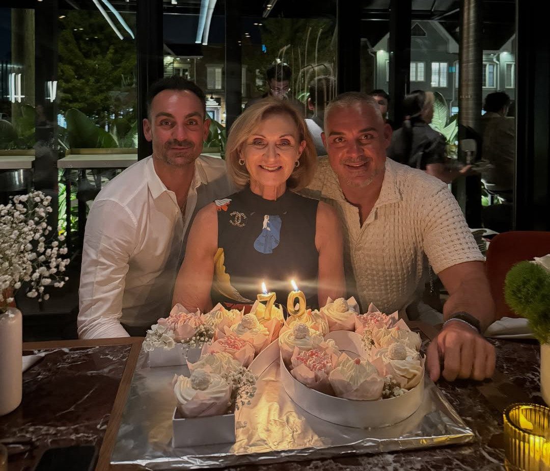 Woman and two men smiling behind a 70th birthday cake at a restaurant.